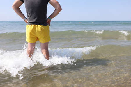 Lifeguard man in yellow shorts stands in sea water and looks into distance. Rule of safe behavior on...