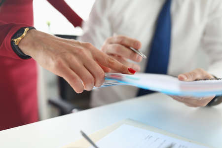 Mans hand holds notebook with pen next to a woman stands and points a finger. Workflow discussion conceptの写真素材