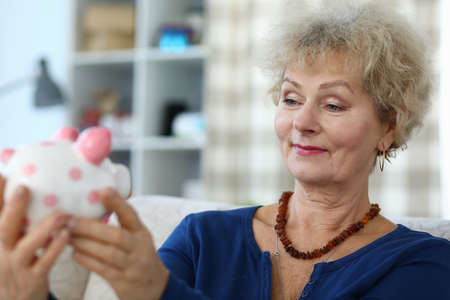 An elderly woman holds piggy bank in her hands and smiles. Pension Font and Accumulation Conceptの写真素材