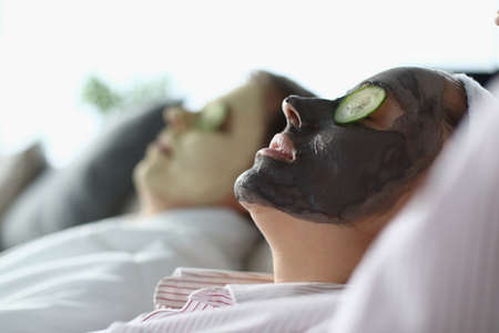Man and woman lie with cosmetic mask on their faces and slices of cucumbers on their eyes. Facial treatments in beauty salons conceptの写真素材