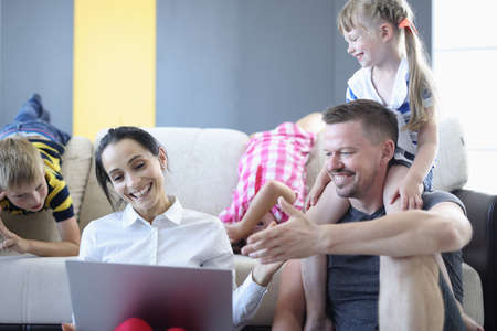 Man and woman and their children are smiling and laughing while sitting on floor and looking at...