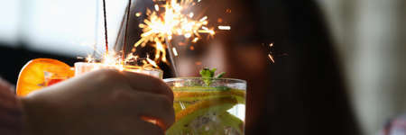 Close-up of friends hands holding fruit cocktails with sparklers decoration. Delicious refreshing beverage. Christmas, new year celebration party and holiday conceptの写真素材