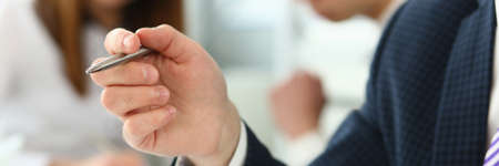 Focus on male hand holding writing pen and wearing classy suit and striped tie. Smart people talking about business project and strategy. Company meeting concept. Blurred backgroundの写真素材