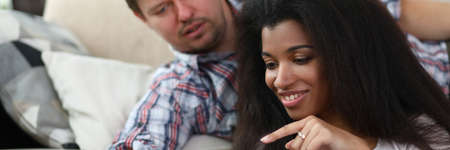Portrait of middle-aged man showing something on mobile phone to woman. Young afro-american female smiling and pointing with finger on screen. Technology and relationship conceptの写真素材