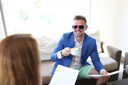 Young smiling man in blue business suit with cup of coffee and document in his hand at meeting with...