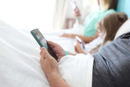 Mom, dad and daughter lie in bed and look at phone. Male hand hold smartphone close up.