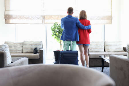 Couple stand in embrace and look out window, rear view. Man and woman wait for plane in lounge.の写真素材