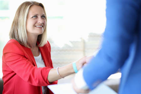 Cheerful woman in red jacket shake hand with man. Colleague greeting and business discussion...