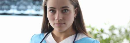 Close-up of young doctor in uniform holding stethoscope. Cute therapist looking at camera with...