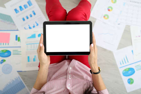 Female hands hold tablet next to graphs with commercial indicators. Remote work and delivery of...