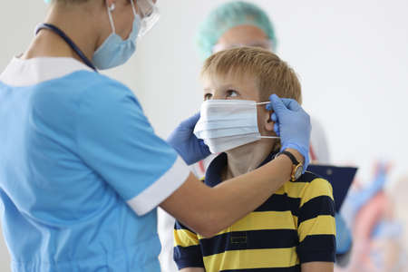 Boy is put on protective medical mask in doctors office. Child health safety in pandemic concept