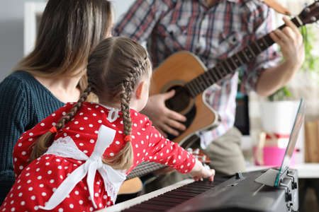 Daughter, father and mother play musical instruments, guitar, pionino together. Family weekend fun...