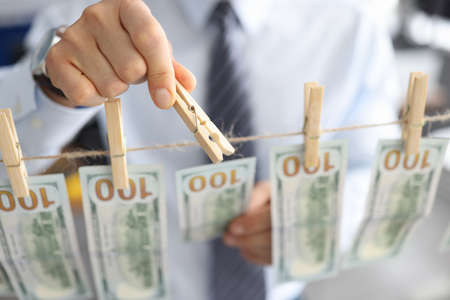 Mans hand of businessman attaches fmerican dollars to rope with clothespins close-up. Business money laundering concept.の写真素材