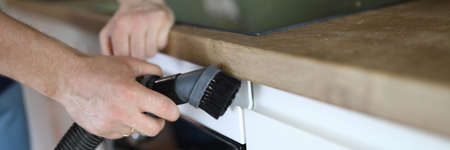 Close-up of man from professional cleaning service clean kitchen furniture with vacuum cleaner....