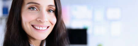 Close-up of cheerful smiling woman posing on camera in office. Macro shot of brunette young female...