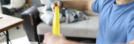 Close-up of person training with yellow fitness rubber band. Indoors gym with necessary equipment...