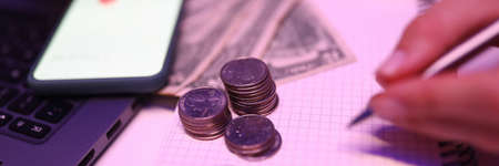 Close-up of person accounting money on mobile phone. Banknotes and coins on table. Detailed...
