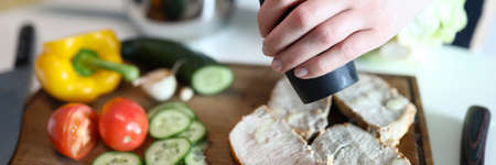 Close-up of woman using pepper for slices of meat. Yellow sweet pepper cucumber and tomato on wooden board. Delicious breakfast. Healthy lifestyle and cuisine conceptの写真素材