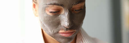 Close-up of young pretty female with clay mask on face. Attractive woman in pyjamas after night...