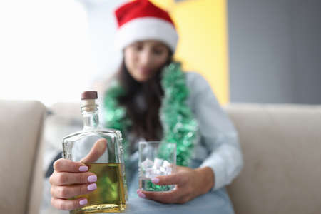 Woman in red santa hat holds a glass of ice and a bottle of whiskey close-up. Celebrating christmas...