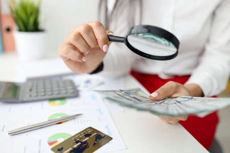 Woman check currency for authenticity. Female hand hold magnifying glass and lot of money. On white...