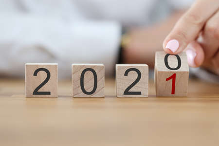 Numbers 2020 make up wooden cubes in row. Female hand turn number 2020 into number 2021 with her...