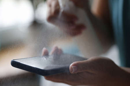 Mobile phone in hands of woman is treated with antiseptic spray close-up. Disinfection of smartphone with antiseptic concept.の写真素材