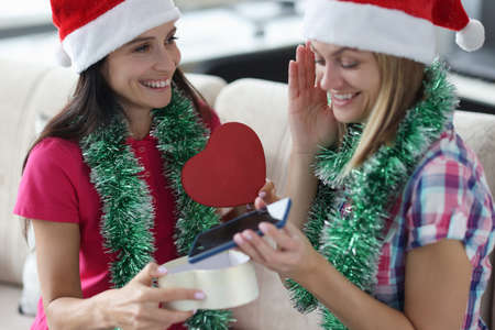 Happy women in red christmas hats give gift box with smartphone. Celebrating christmas and new year in lgbt families concept.の写真素材