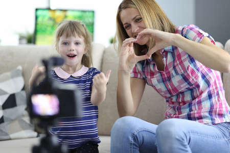 Woman with child is sitting on couch in apartment and showing hand gesture in front of camera. Family business blogging concept.の写真素材