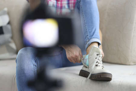 Woman puts on warm boot with her foot on sofa in front of camera close-up. Online earnings blogging...