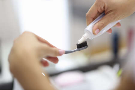 Female hand squeezing toothpaste from tube onto toothbrush close-up. Daily oral care after meals concept.の写真素材