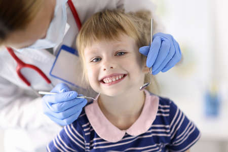 Dentist doctor examines teeth of little smiling girl in clinic. Painless dental treatment for children concept.の写真素材