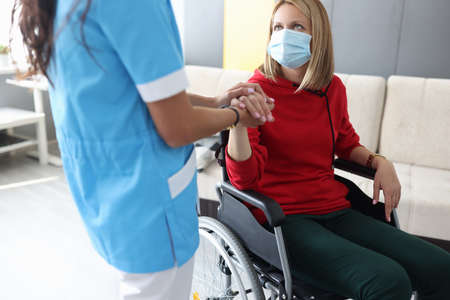 Doctor in uniform holds hand of sick young woman in wheelchair portrait. Psychological assistance to...