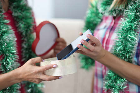 Female hands are holding and passing festive box with smartphone. New Year gifts and surprises...
