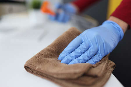 Gloved hand holds microfiber cloth and wipes table. Services of cleaning companies concept
