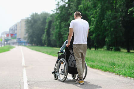 Man rolls wheelchair with girl down street. Relationship with a disabled person and walking together conceptの写真素材