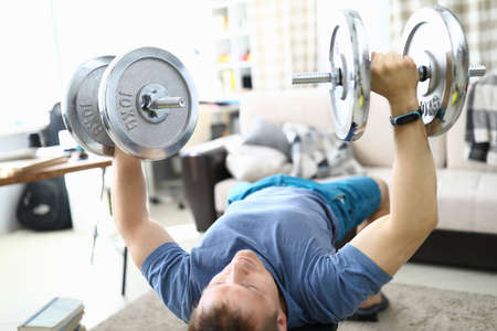 Man at home raises barbell and shakes his biceps. How to stay fit in the coronavirus pandemic conceptの写真素材
