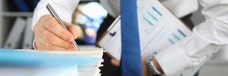 Close-up of employee finish annual report for conference meeting. Businessman holding clipboard with diagrams. Man in trendy costume in company office. Business conceptの写真素材