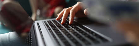 Close-up of person working on laptop sitting on sofa. Young woman typing on grey modern gadget....