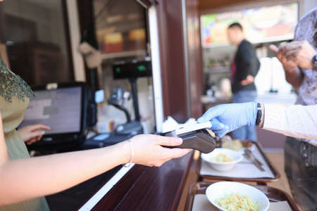 Hand in protective glove holds a bank card cashier holds out terminal for payment. Payment by bank cards in a pandemic conceptの写真素材