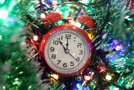 Red alarm clock lying on table in bright garland and tinsel closeup. Crown of new year and christmas...