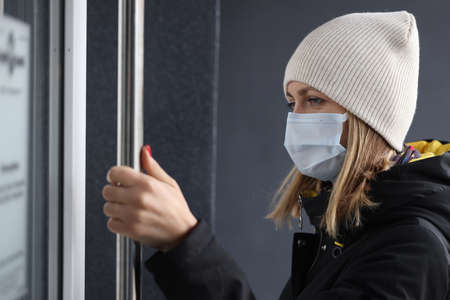 Young woman in protective medical mask and warm clothing opening door to store. Being in public...