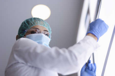 Doctor in glasses and medical mask and gloves is holding an X-ray picture. International medical...