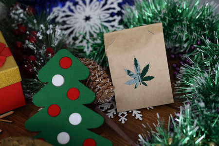 Paper bag with marijuana grass lying among Christmas tree decorations and toys close-up. Illegal new...