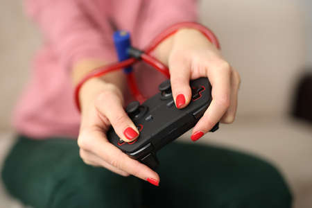 Young woman holding in hands tied with rope joystick from video games computer close-up. Mental...