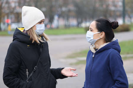 Two women in medical protective masks communicate in street. Safe walks in coronavirus pandemic...