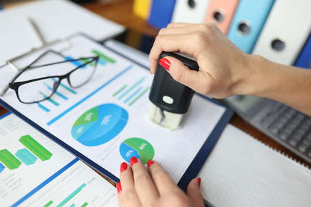 Woman puts stamp on documents with commercial indicators. Checking business performance in an enterprise conceptの写真素材