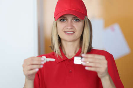 Woman in red uniform holds a key and lock in her hands. Lock picking services and service concept