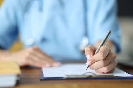 Doctor holding in hand silver pen on documents at table in office close-up. Documentation in...