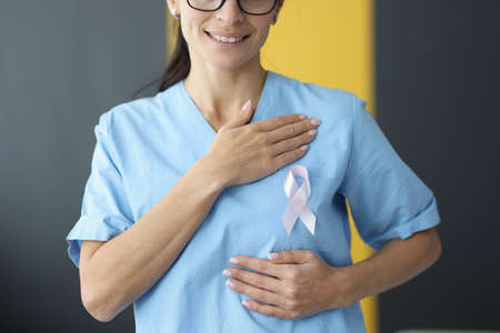 Doctor holding pink ribbon in hand near chest in clinic close-up. World day against breast cancer...